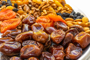 Dates, dried apricots, raisins lie on a silver tray on a white wooden background, side view from above