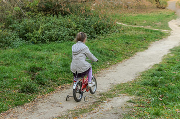 Naklejka premium Little happy girl child rides a bicycle in the autumn forest