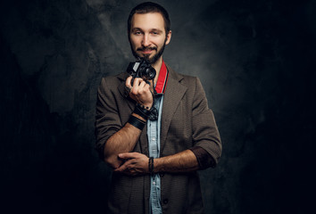 Attractive pensive man with photo camera is posing for photographer at dark photo studio.