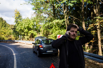 A broken car on the road, the driver holds an open hood and watches what has broken down, a roadside assistance is waiting