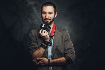 Attractive pensive man with photo camera is posing for photographer at dark photo studio.