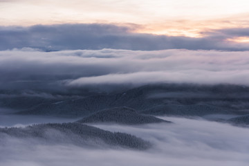 Magic winter fogs in Ukrainian Carpathians overlooking the snow-capped mountain peaks from the picturesque mountain valley with tourists in tents.