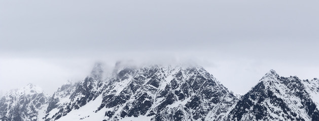 Rocky mountains in snow and overcast grey sky at winter