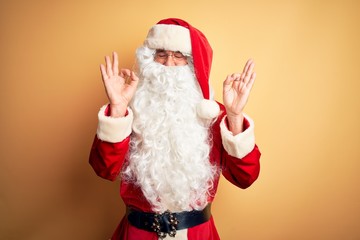 Middle age handsome man wearing Santa costume standing over isolated yellow background relax and smiling with eyes closed doing meditation gesture with fingers. Yoga concept.