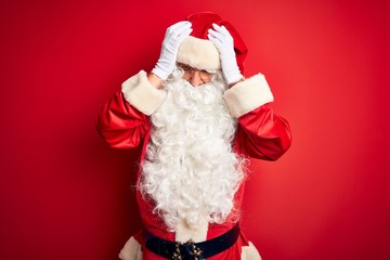 Middle age handsome man wearing Santa costume standing over isolated red background suffering from...