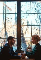 Happy smiling couple of attractive people sitting and cafe and warming up with coffee.