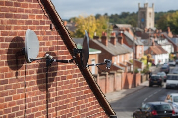 Two satellite dishes mounted on a brick house wall with a city background