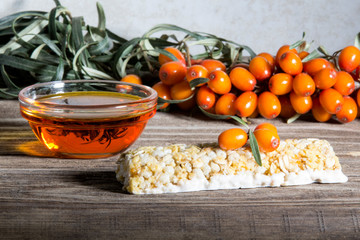 Energy bar with sea buckthorn berries on a wooden background. Sea buckthorn berries on a branch and sea buckthorn oil in a glass Cup.