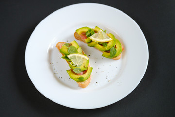 oasts with avocado salmon, basil leaves and a slice of lemon on a black background. healthy breakfast concept.