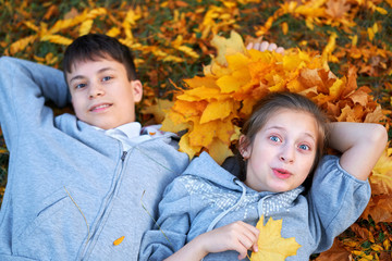 Girl and boy teenager having holiday in autumn city park, lying on grass, posing, smiling, playing and having fun. Bright yellow trees and leaves