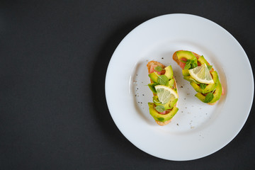 oasts with avocado salmon, basil leaves and a slice of lemon on a black background. healthy breakfast concept.