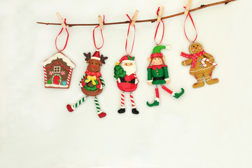 Christmas tree decorations hanging on a branch with santa claus, reindeer, elf, gingerbread house and cookie lady on cream background with copy space.