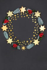Christmas wreath abstract decoration with gold stars and baubles, holly and winter flora on dark grey background with copy space. Decorative symbol for the festive season.