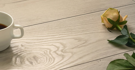 yellow flower rose and part of cup of coffee on wooden desktop background