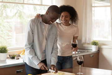Happy wife standing with glass of wine near cooking husband.