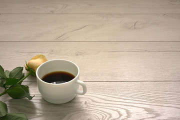 one yellow tea rose and cup of black coffee on wooden desktop