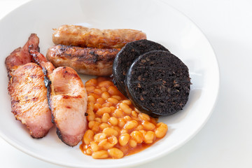 Cumberland sausages, bacon, baked beans and black pudding in a white bowl