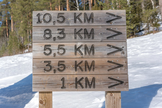 close-up wooden signage with pointing distance in kilometer snow forest background