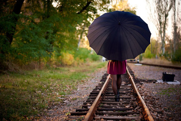 A girl with a black umbrella is walking on the railway.