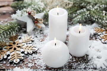 Christmas candles with snowflakes and fir tree branches on brown wooden table