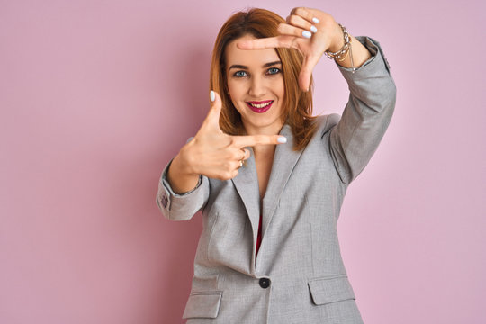 Young caucasian business woman wearing a suit over isolated pink background smiling making frame with hands and fingers with happy face. Creativity and photography concept.