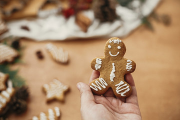Gingerbread man cookie in hand on background of anise, cinnamon, pine cones, cedar branches on rustic table. Merry Christmas. Atmospheric image. Baked christmas cookie