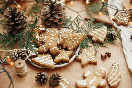 Christmas gingerbread cookies on vintage plate and anise, cinnamon, pine cones, cedar branches  with golden lights on rustic table. Baked traditional gingerbread man, tree, star cookies