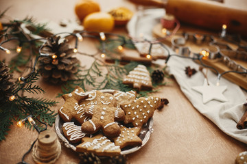 Christmas gingerbread cookies on vintage plate and anise, cinnamon, pine cones, cedar branches  with golden lights on rustic table. Baked traditional gingerbread cookies. Seasons greetings