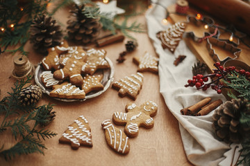 Christmas gingerbread cookies on vintage plate and anise, cinnamon, pine cones, cedar branches  with golden lights on rustic table. Baked traditional gingerbread cookies. Seasons greetings