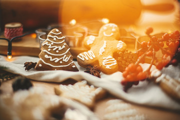 Festive gingerbread man and christmas tree cookies on background of wooden rolling pin, anise, cinnamon, pine cones, golden lights bokeh on rustic table. Merry Christmas. Atmospheric