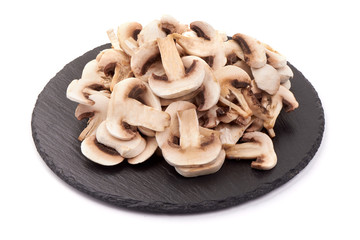 Fresh sliced champignon mushrooms on a stone plate, isolated on white background