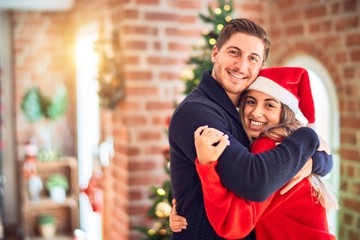 Young beautiful couple smiling happy and confident. Standing and hugging around christmas tree at...