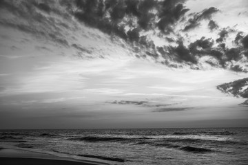 Dramatic clouds hang over the ocean at sunrise in this black and white photo