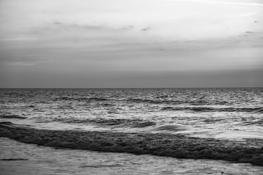 Clouds hang over the ocean at sunrise in this black and white photo o choppy waves