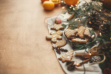 Fototapeta premium Merry Christmas. Festive gingerbread cookies with anise, cinnamon, pine cones, cedar branches and golden lights bokeh on rustic table. Space for text. Atmospheric image.