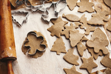 Making christmas gingerbread man cookies. Raw dough in shape of  tree and man and metal cutters, wooden rolling pin, anise, ginger, cinnamon, pine cones, fir branches on rustic table. - Powered by Adobe