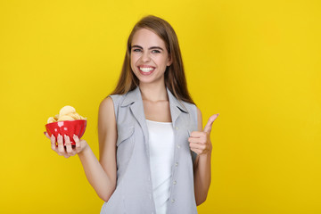 Young beautiful girl with potato chips in bowl on yellow background