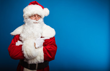 I choose you! Authentic Santa Claus is posing with his arms folded, looking somewhere to the right, pointing with his right hand to the copyspace nearby.