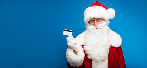 Modern Santa. Authentic Santa Claus is posing, showing a credit card, which he holds in his right hand in a white glove, while looking at the camera.