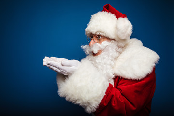 St. Nicolas. Authentic Santa is posing in profile, holding his hands together and his palms facing up, looking to the left and blowing an air kiss.