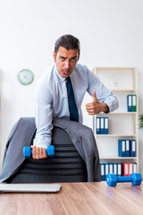 Young handsome employee doing sport exercises at workplace