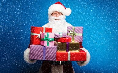 Santa's work. Happy beautiful Santa Claus in red costume is posing and holds a lot of gift boxes for children.
