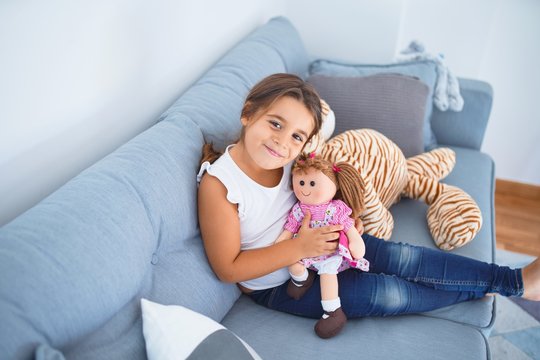 Adorable toddler smiling happy. Sitting on the sofa hugging doll at home
