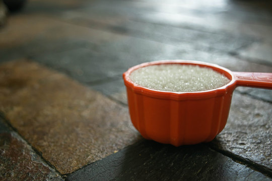 Measuring cup with sugar on dark surface