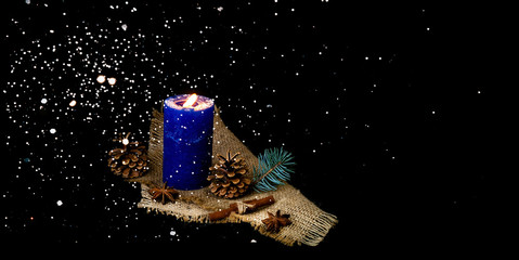 Blue candle on burlap texture. Christmas decor with falling snow. Blurred effect. Top view, copy...