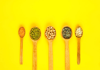 Wooden spoons with various cereals on yellow background. Various vegan ingredients. Close-up