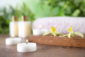 Fototapeta na wymiar Composition with burning candles and flowers on wooden table against blurred background, space for text. Spa concept