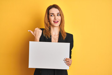 Naklejka premium Redhead business caucasian woman holding banner over yellow isolated background pointing and showing with thumb up to the side with happy face smiling