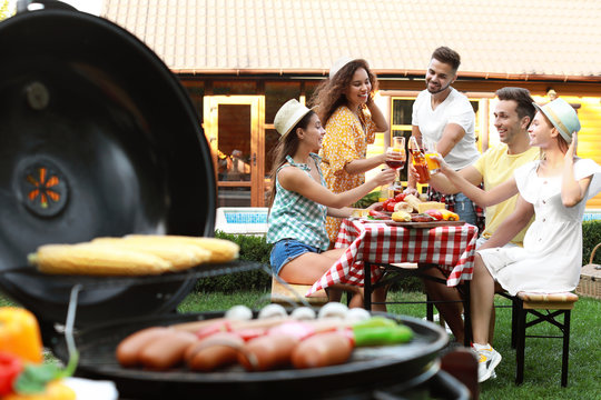 Group of friends at barbecue party outdoors. Blurred view of grill with sausages and vegetables