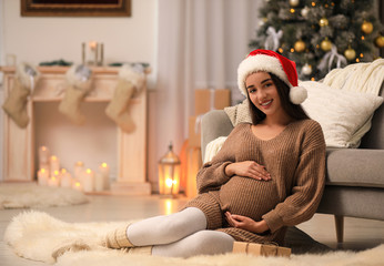 Happy pregnant woman with Christmas gift box at home. Expecting baby